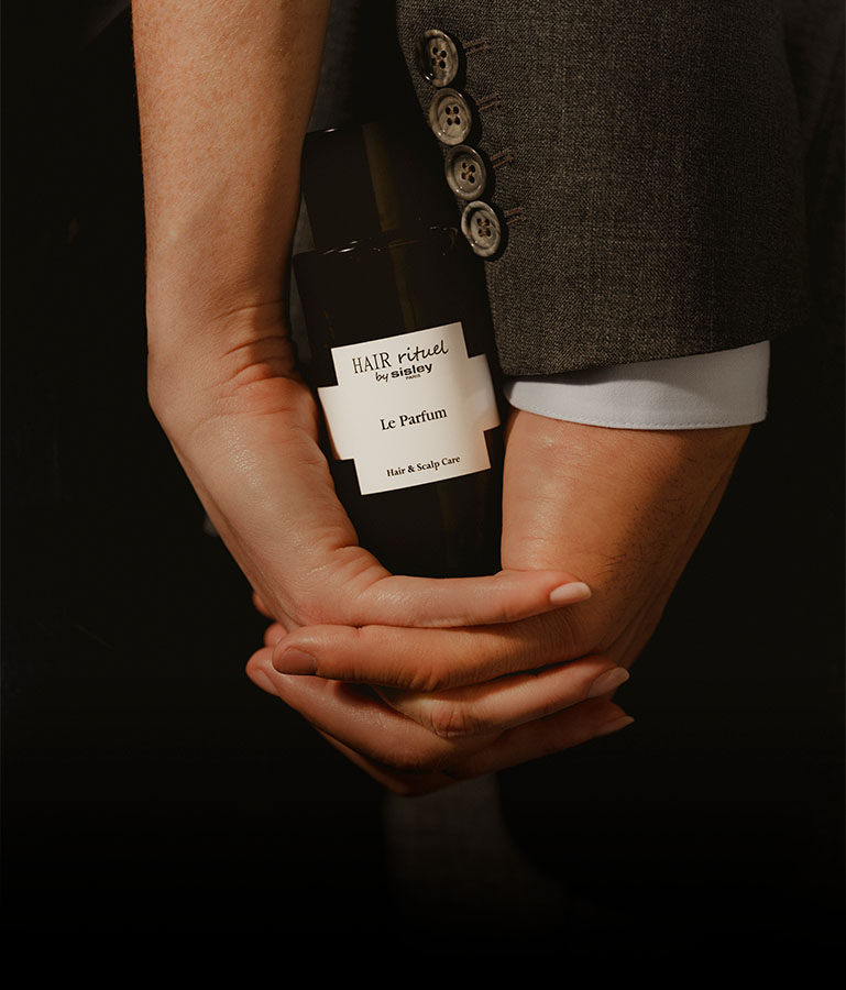 Hombre y mujer sosteniendo en sus manos enlazadas el frasco de Le Parfum Hair Rituel de Sisley